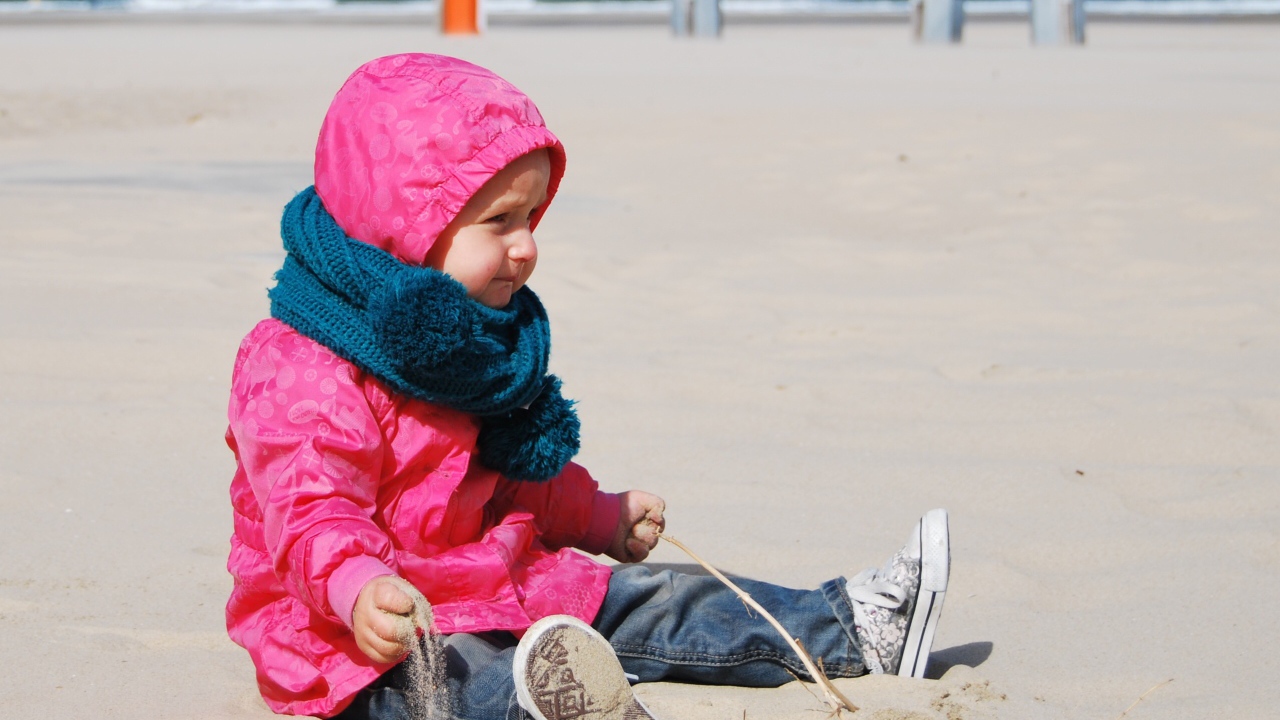 Маленькая девочка в розовой куртке на песке