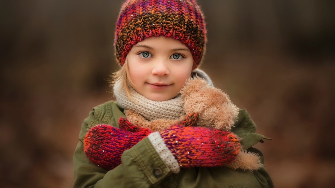 Маленькая девочка в теплой шапке и варежках  с игрушкой в руках 