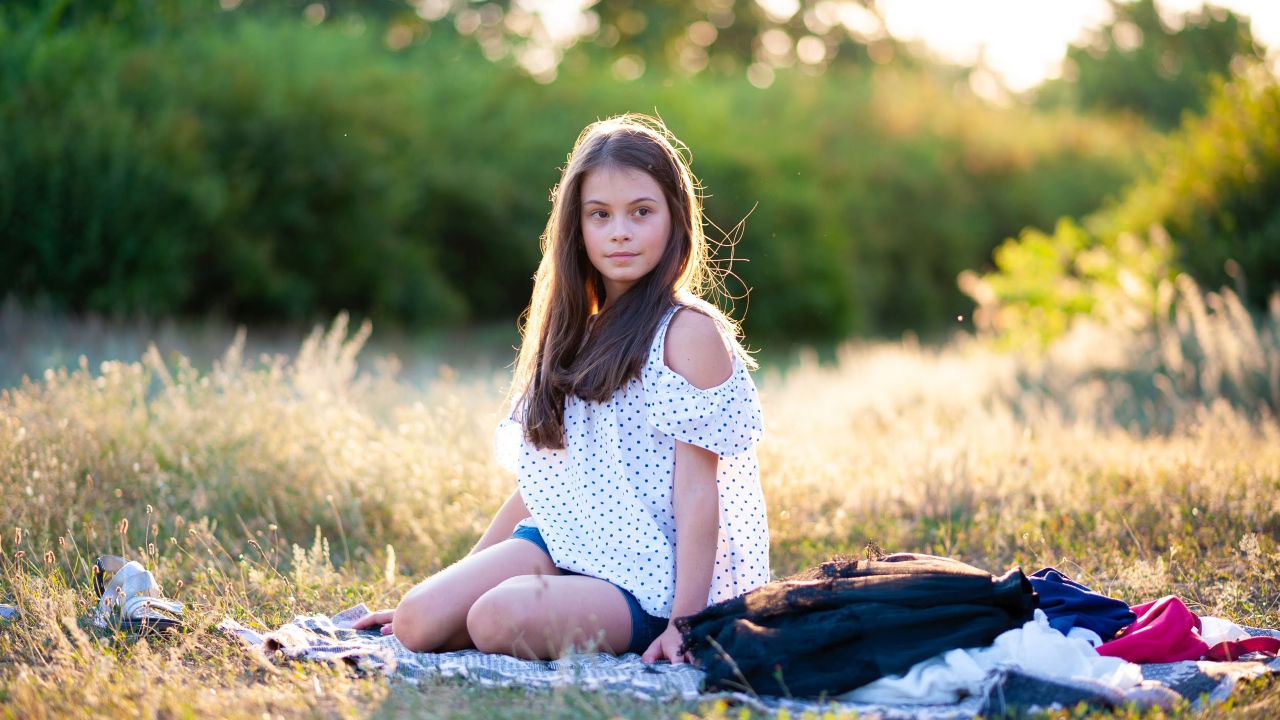 Маленькая девочка сидит на покрывале на земле 