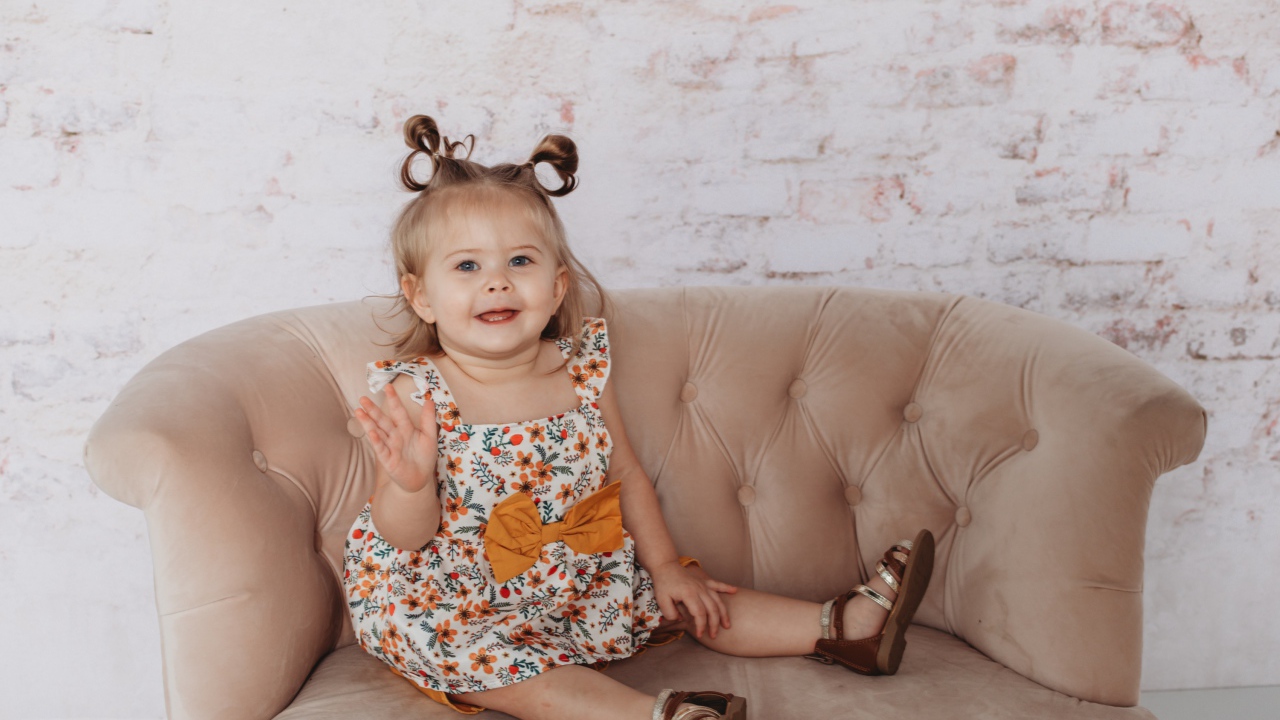 Маленькая девочка сидит на диване у стены