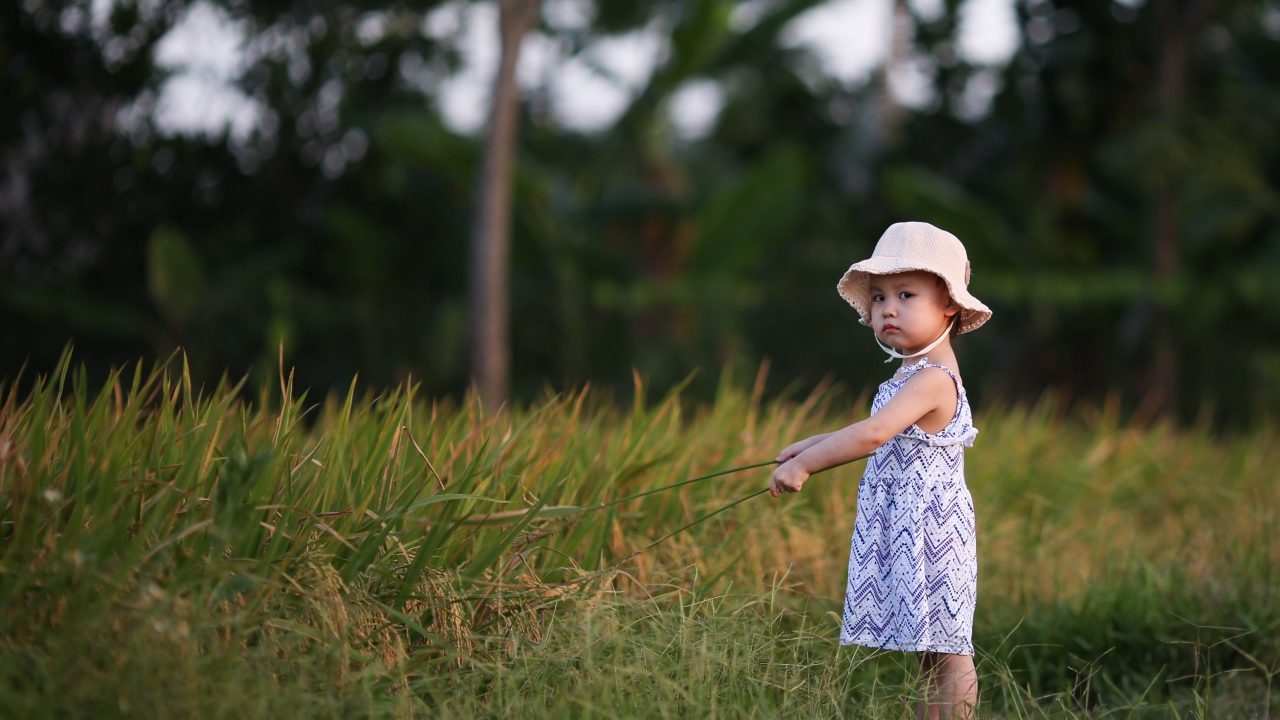 Маленькая девочка с панамой на голове  стоит в траве
