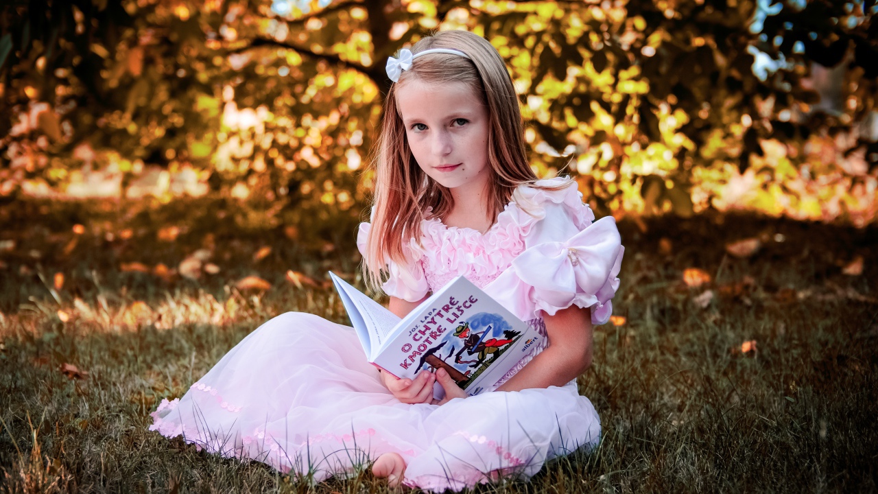 Маленькая принцесса сидит на траве с книгой