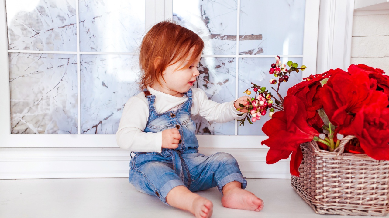 Маленькая рыжеволосая девочка сидит у корзины цветов 