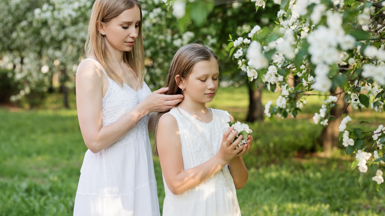 Мама заплетает дочке волосы у дерева