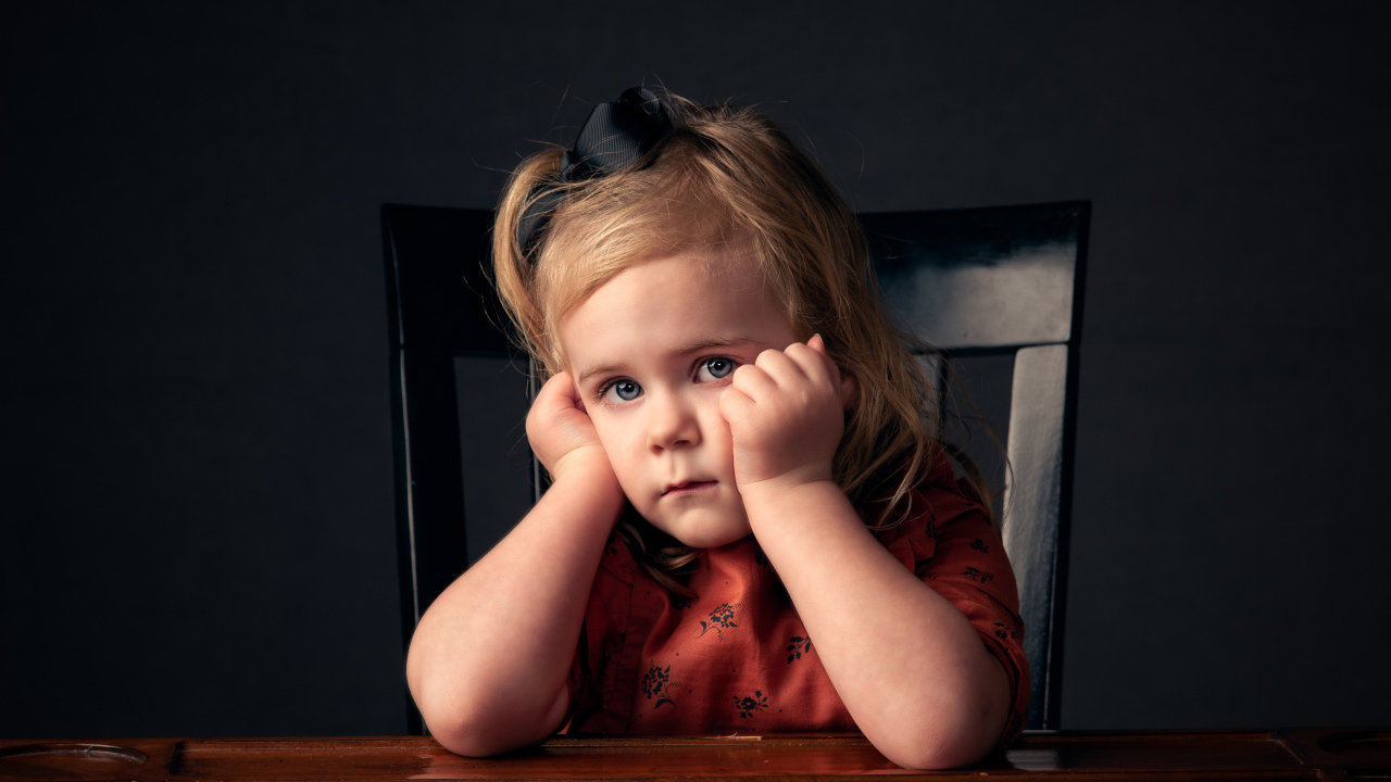 Грустная маленькая девочка сидит на черном стуле