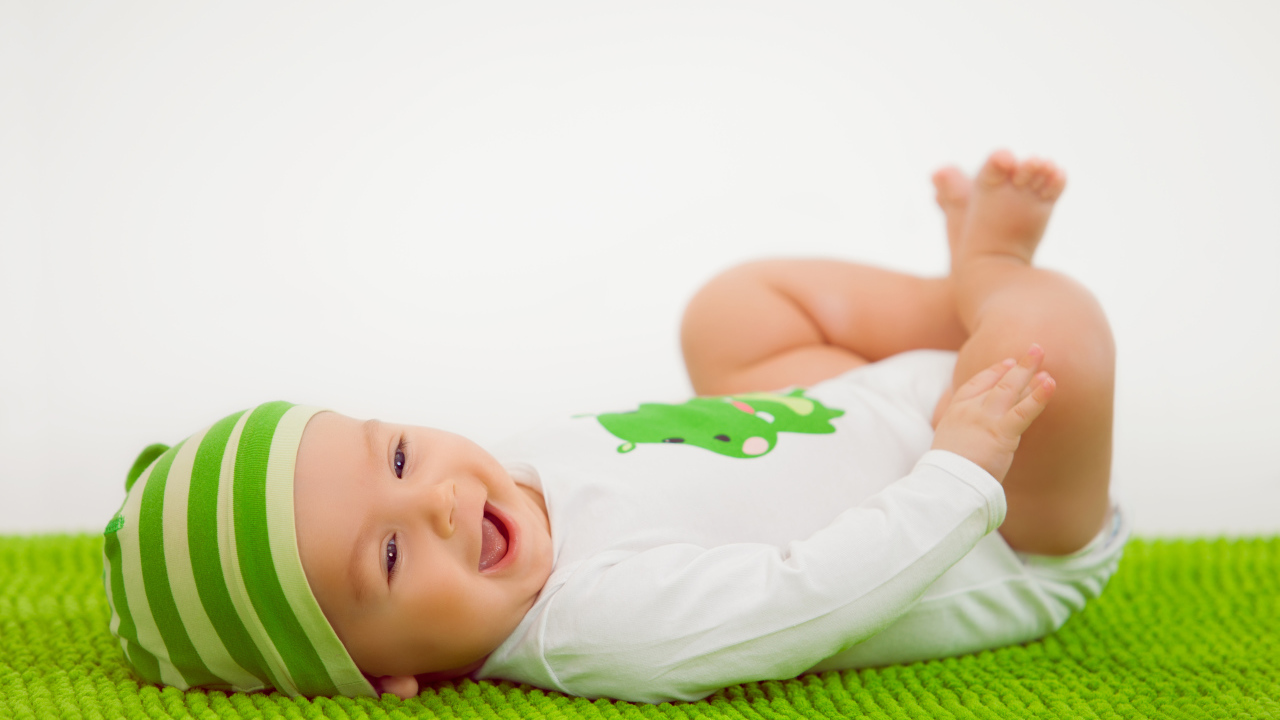 Улыбающийся маленький ребенок лежит на зеленом покрывале 