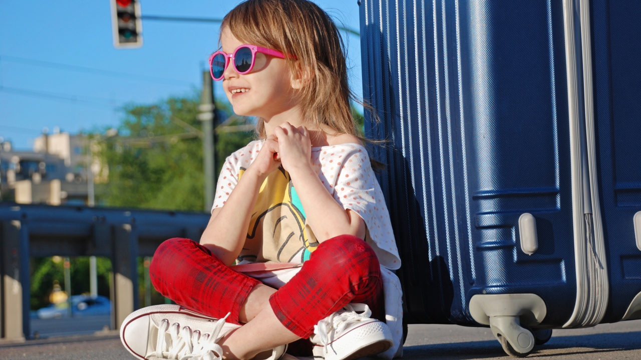 Улыбающаяся маленькая девочка в очках с чемоданом