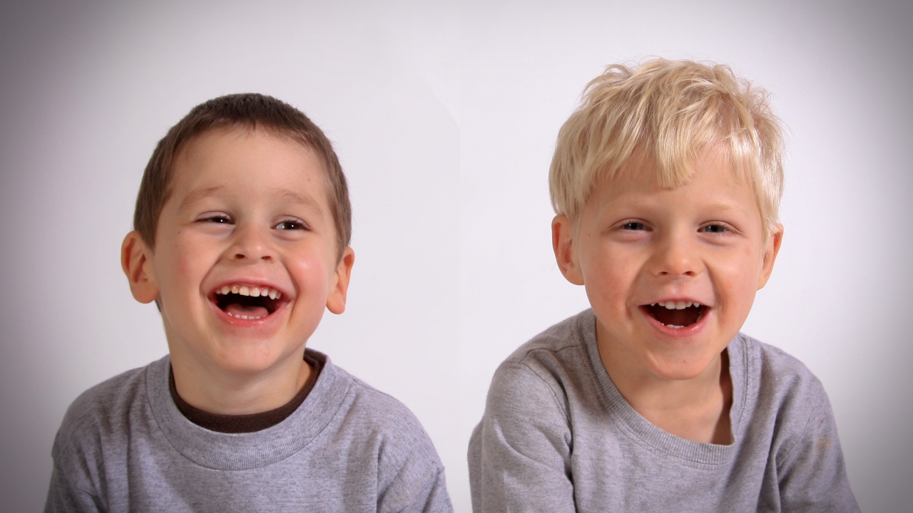 Два маленьких мальчика смеются на сером фоне