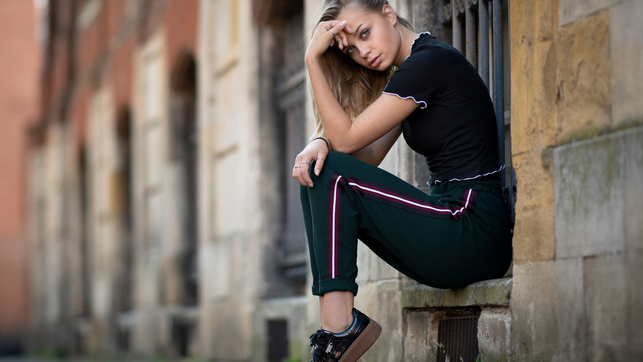 Девушка в спортивном костюме сидит у здания