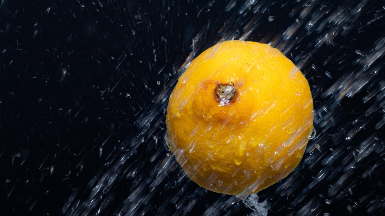 Лимон в брызгах воды на черном фоне
