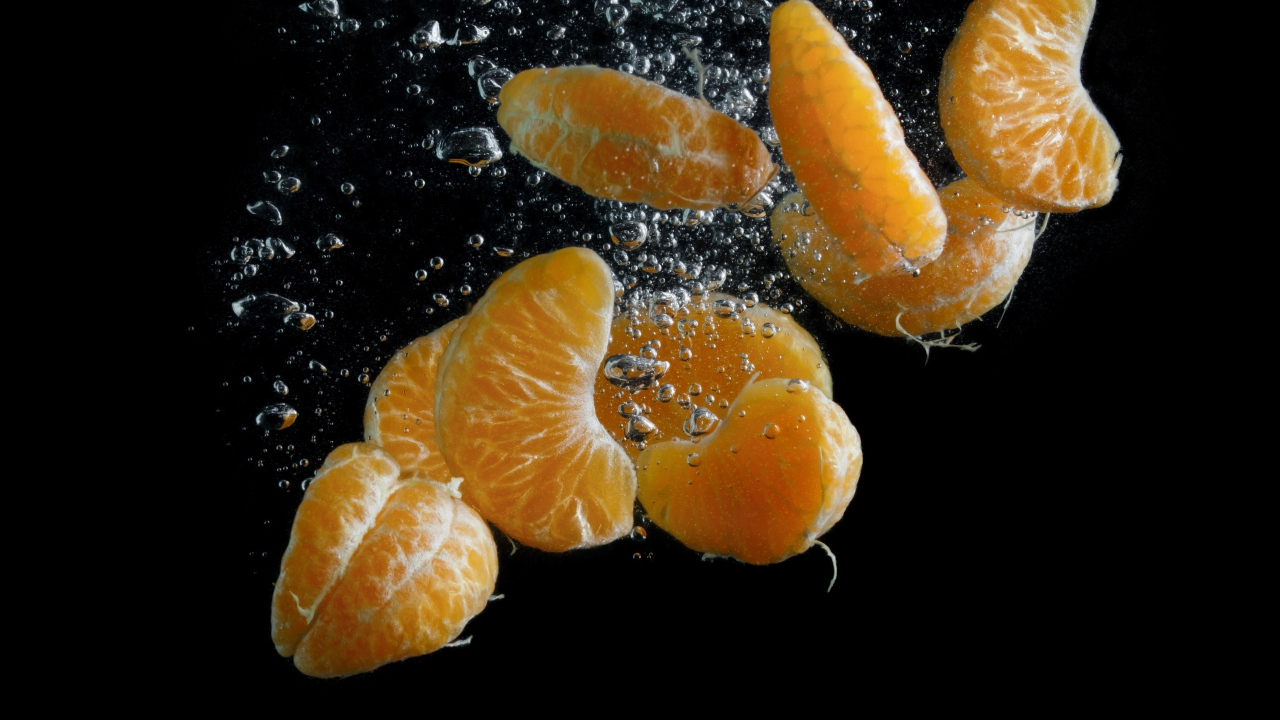 Дольки мандарина в воде на черном фоне