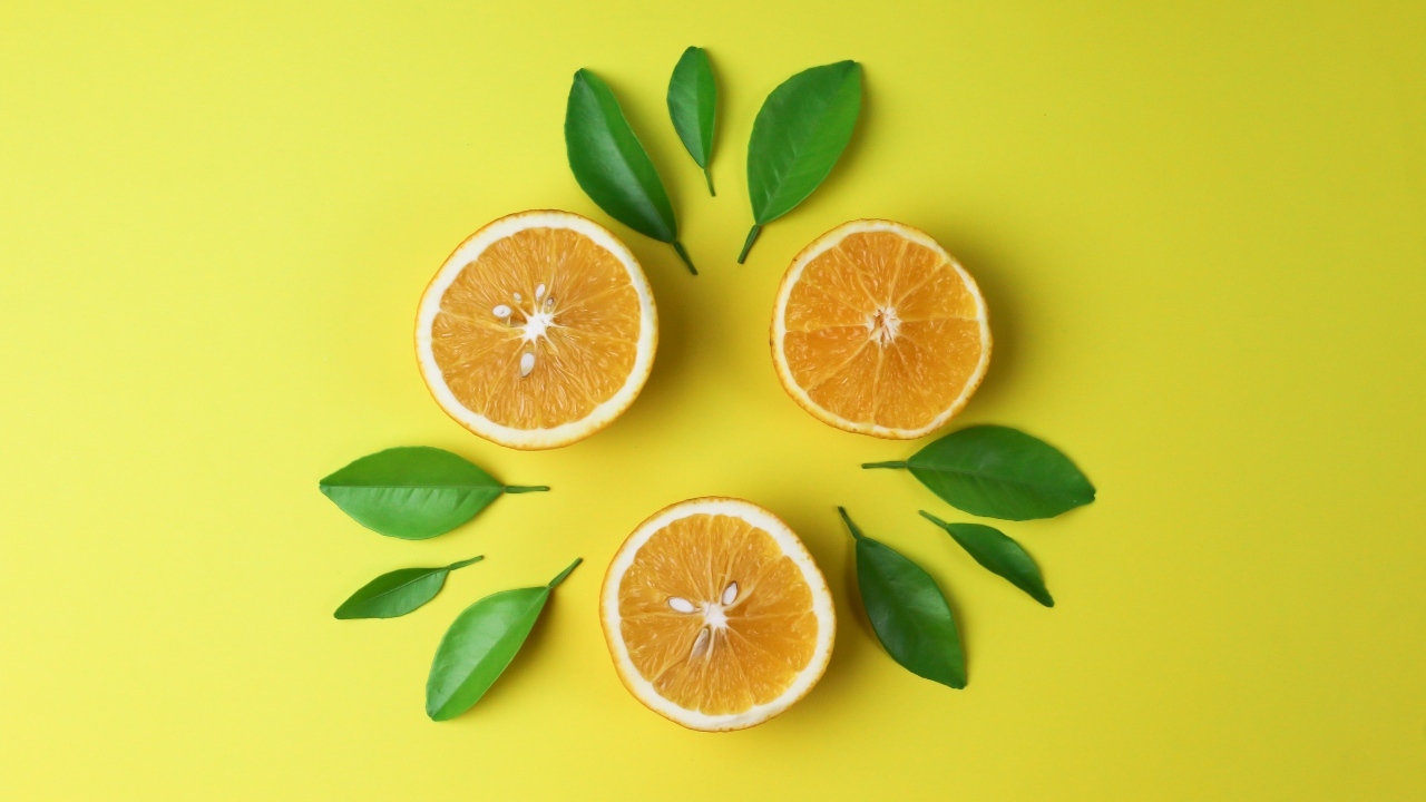 Половинки апельсина с зелеными листьями на желтом фоне