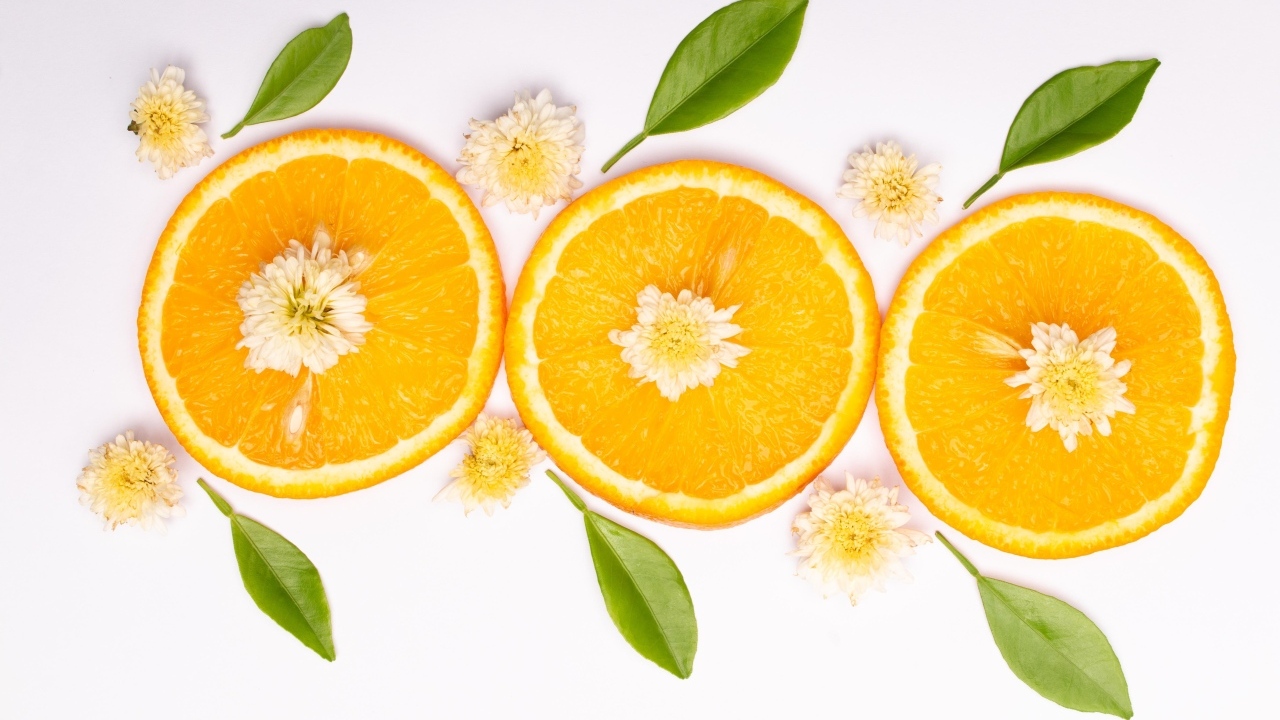 Три кружочка апельсина на белом фоне с цветами и зелеными листьями