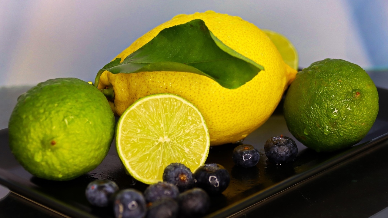 Желтый лимон на тарелке с лаймом и ягодами черники 
