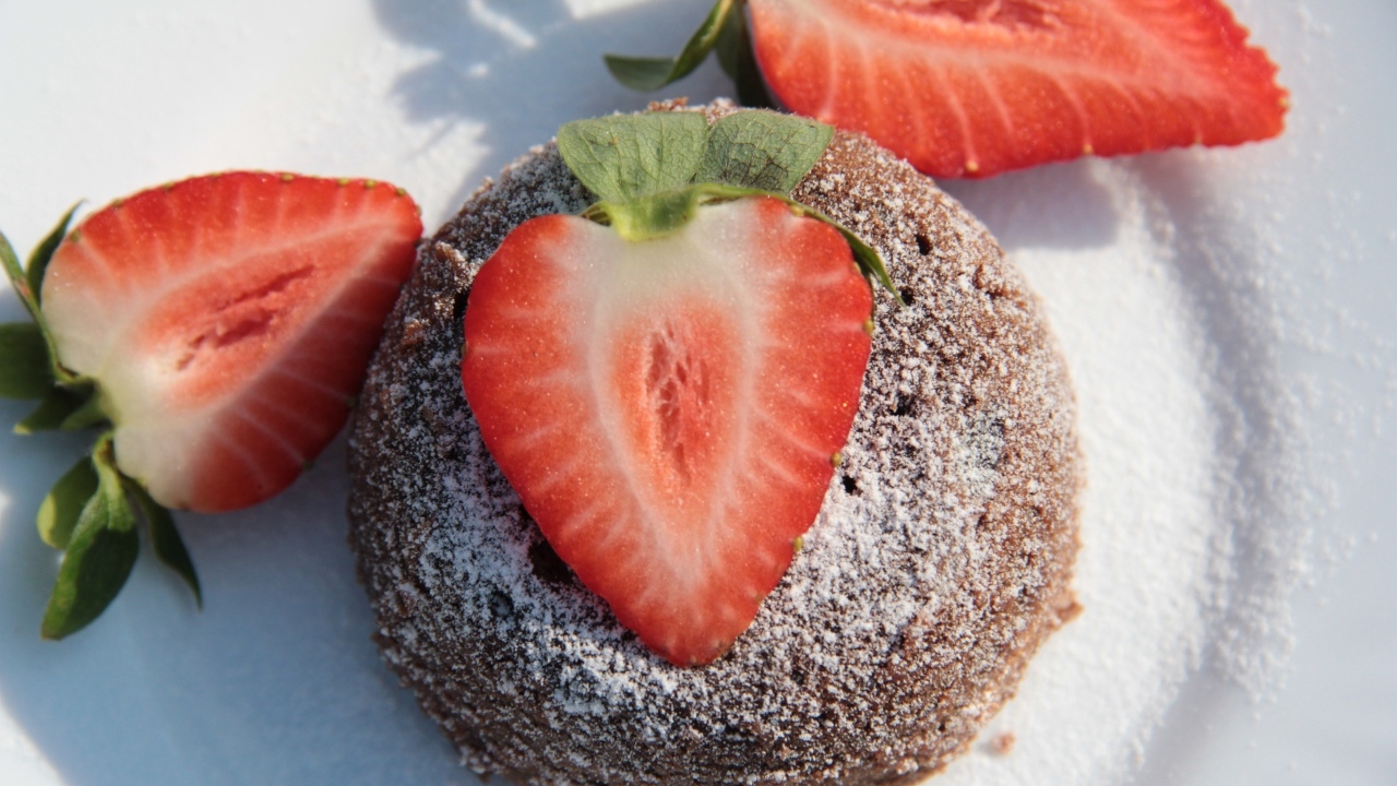 Пирожное на  тарелке с клубникой и сахарной пудрой