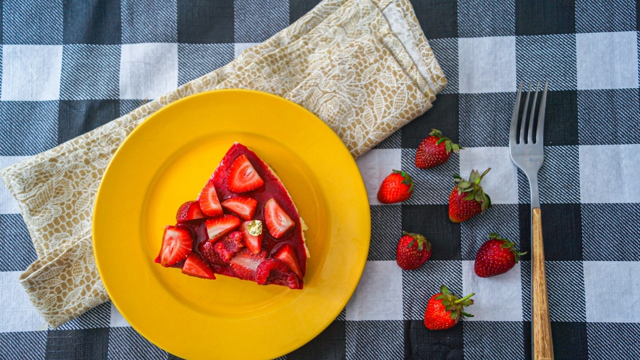 Кусок чизкейка с клубникой на желтой тарелке 