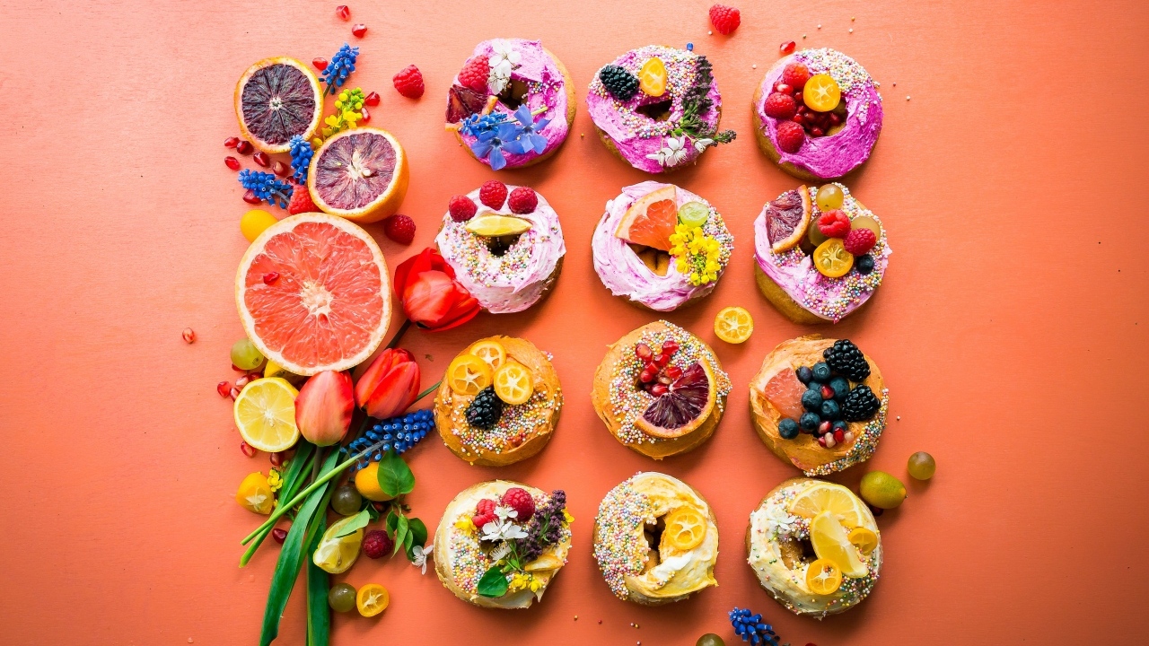 Сладкие пончики на оранжевом фоне с фруктами и цветами