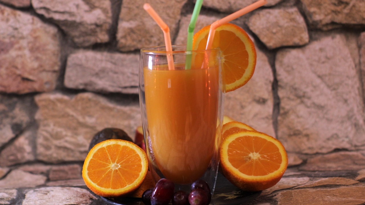 Стакан свежего сока с трубочками на столе с апельсинами