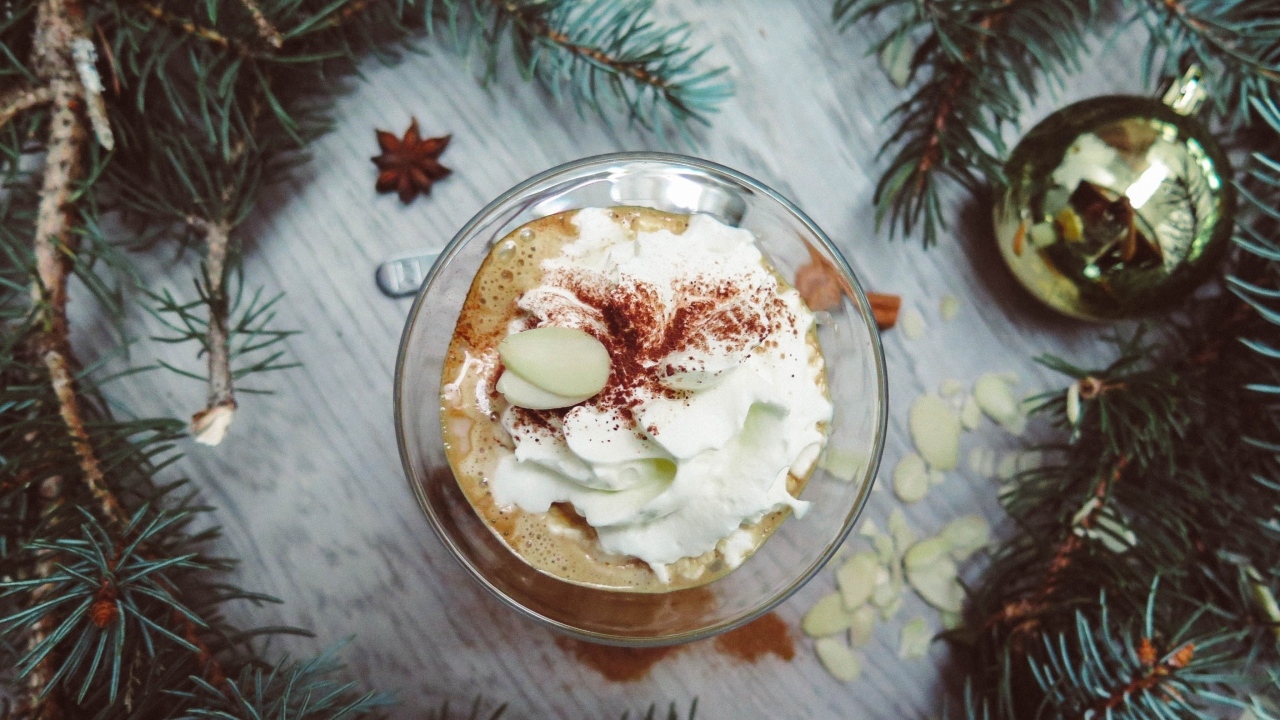 Горячий кофе с взбитыми сливками в чашке на столе с еловыми ветками