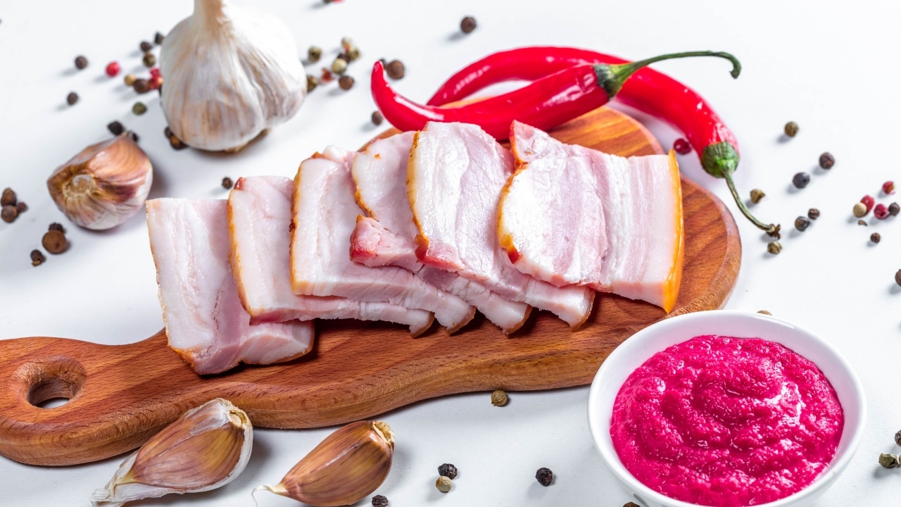 Нарезанное сало на столе с чесноком, хреном и красным перцем