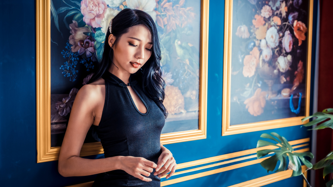 Красивая девушка азиатка в черном платье стоит у картины 