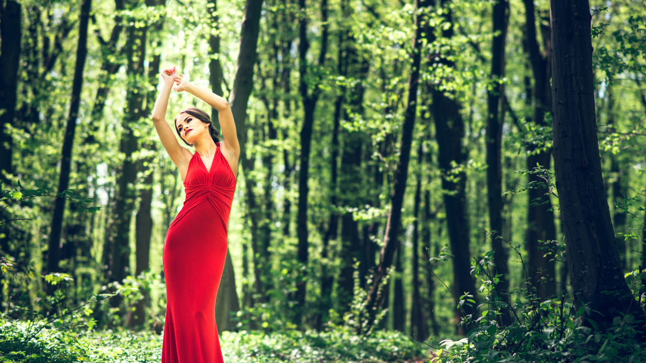Девушка в красивом красном платье стоит в лесу