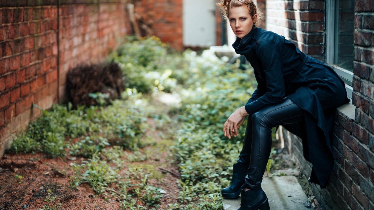 Девушка в черном наряде сидит на окне