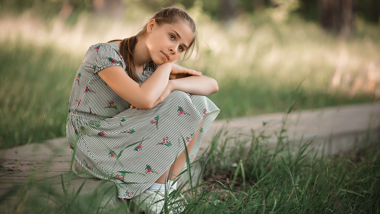 Девушка в платье сидит у зеленой травы