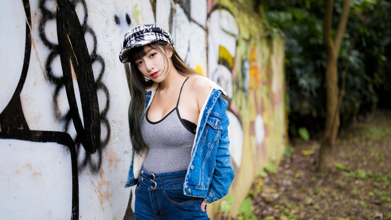 Девушка азиатка в джинсовой куртке стоит у стены