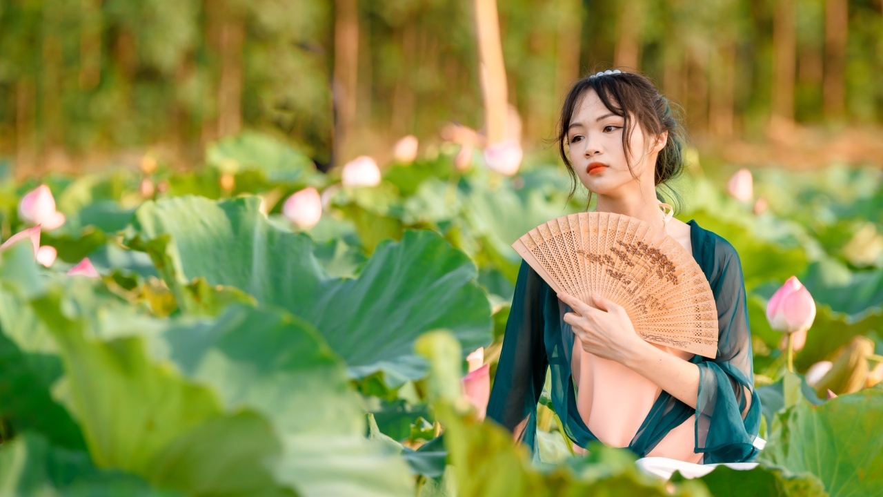 Девушка азиатка с веером в зеленых листьях лотоса