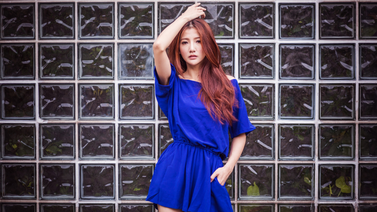 Азиатка в синем платье стоит у стеклянной стены