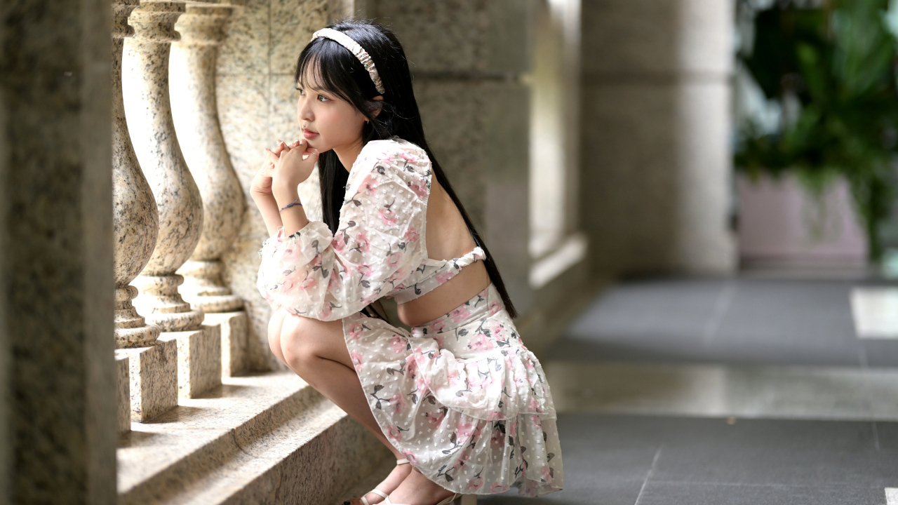 Красивая девушка азиатка в костюме сидит у стены