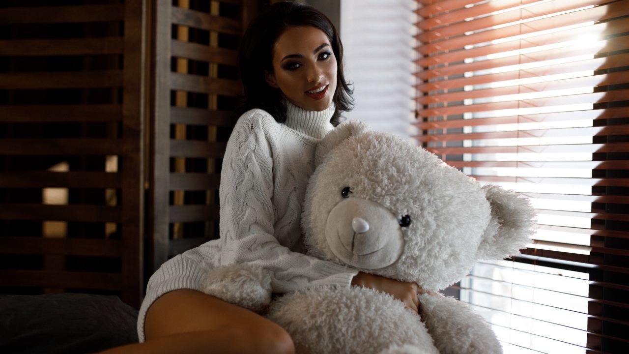 Красивая девушка в свитере с медведем у окна