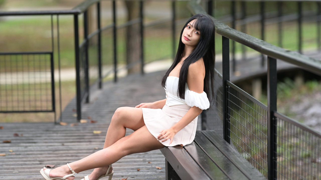 Красивая длинноволосая азиатка в белом платье сидит на лавке