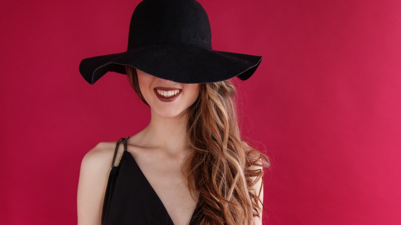 Черная шляпа на лице у девушки на розовом фоне