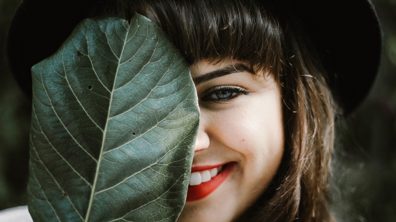 Милая улыбающаяся девушка прикрыла лицо листом