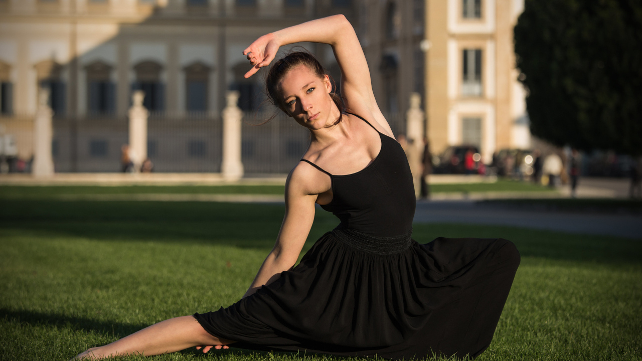 Девушка гимнастка в черном платье на зеленой траве