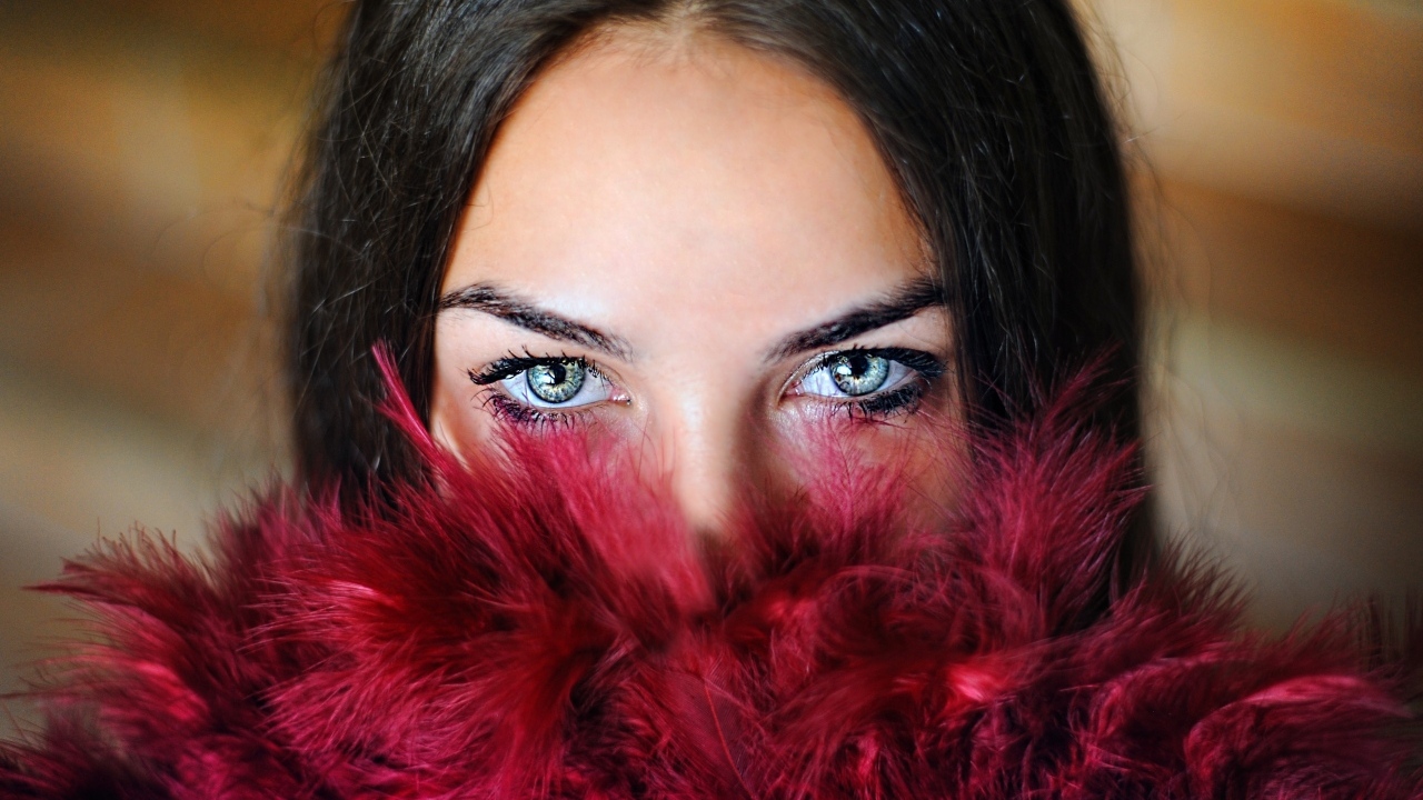 Девушка с красивыми глазами закрыла лицо красными перьями