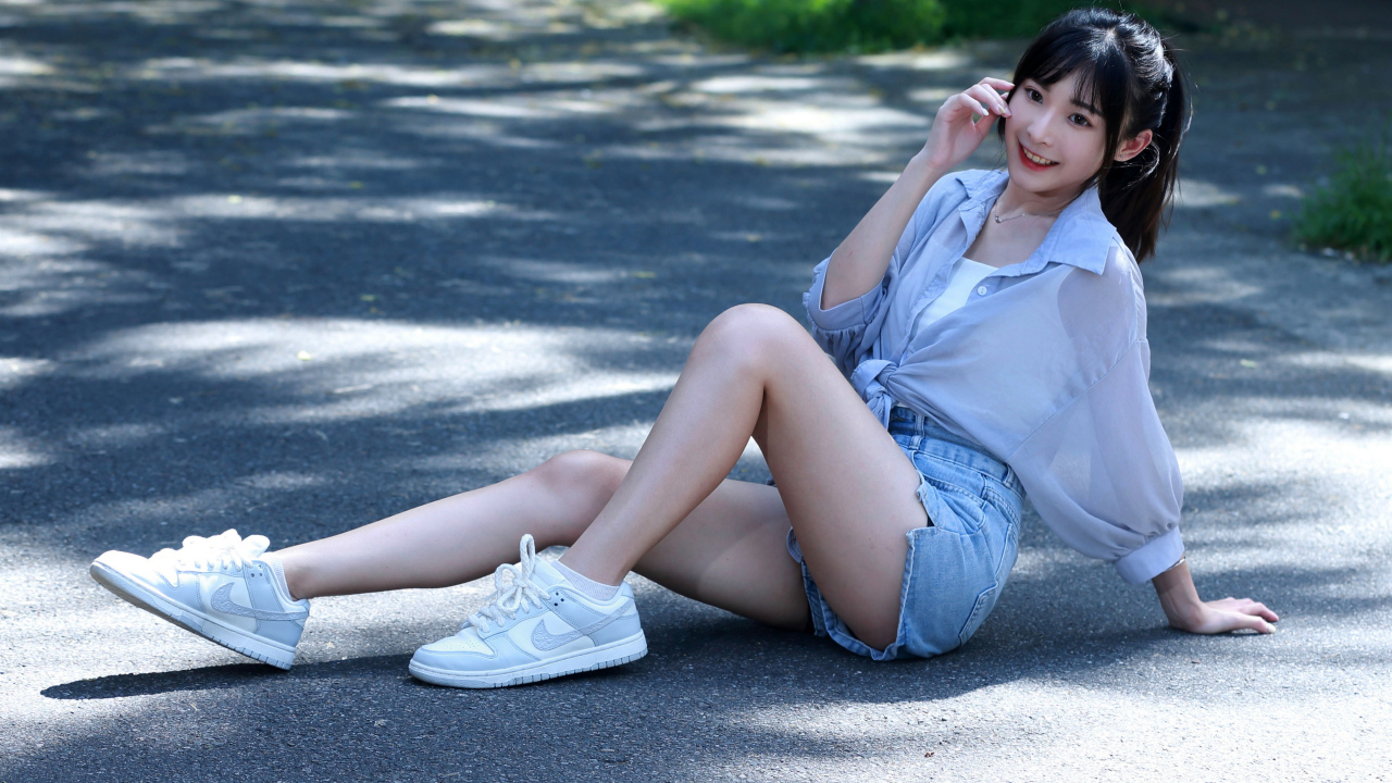 Улыбающаяся девушка азиатка в кедах сидит на дороге
