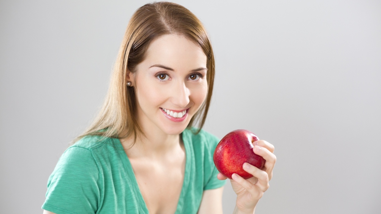 Улыбающаяся девушка с красным яблоком в руках