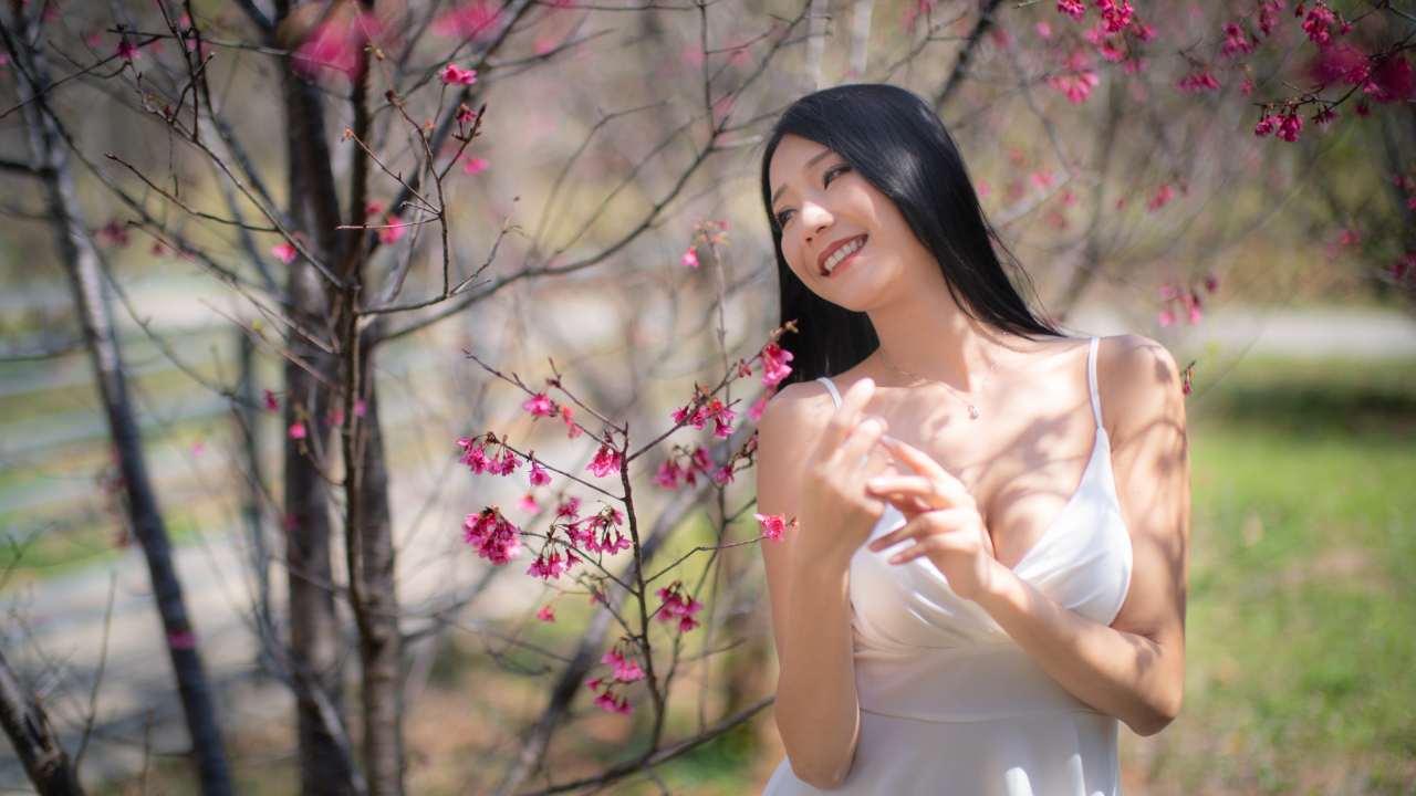 Улыбающаяся девушка в белом платье у дерева с цветами