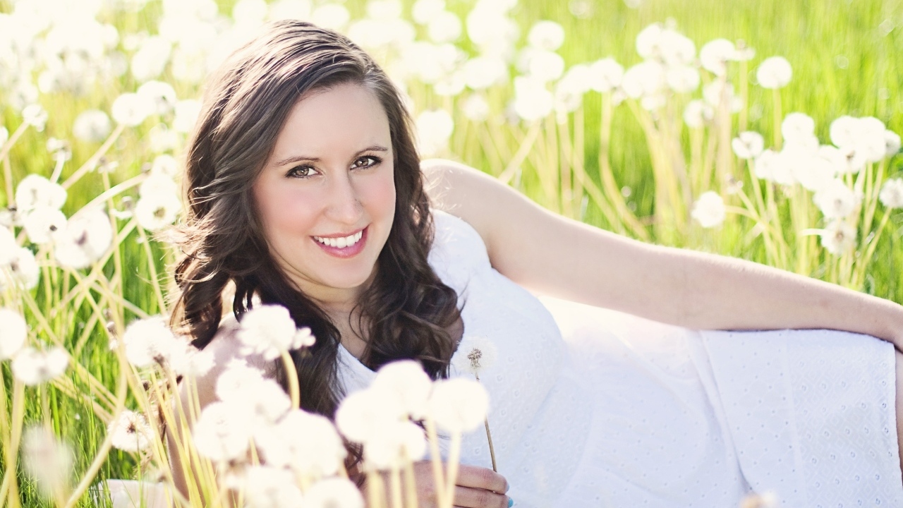 Улыбающаяся девушка лежит на поле с одуванчиками