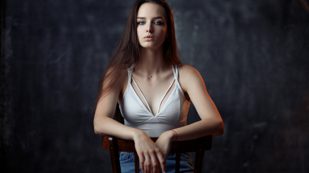 Молодая длинноволосая девушка сидит на деревянном стуле