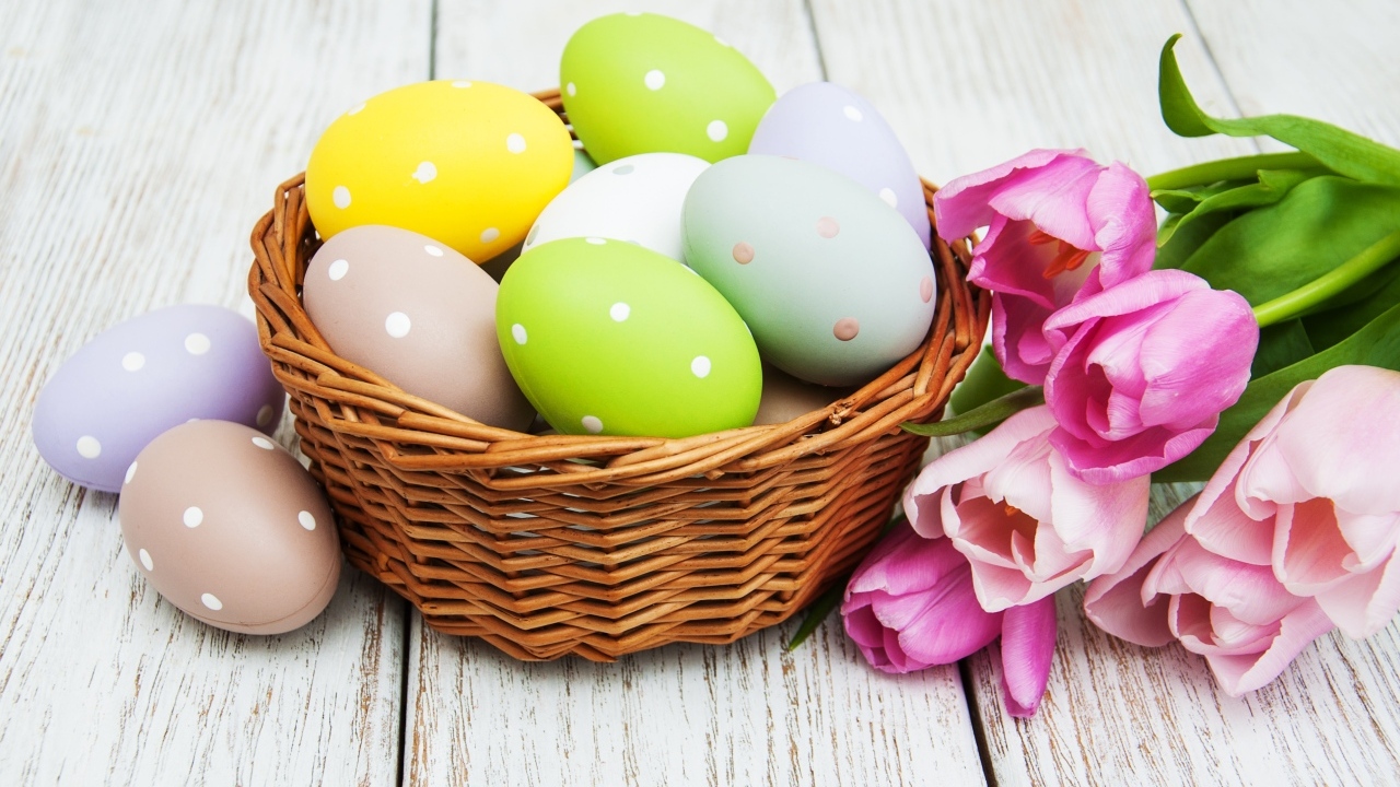Корзина разноцветных яиц с тюльпанами на столе на Пасху