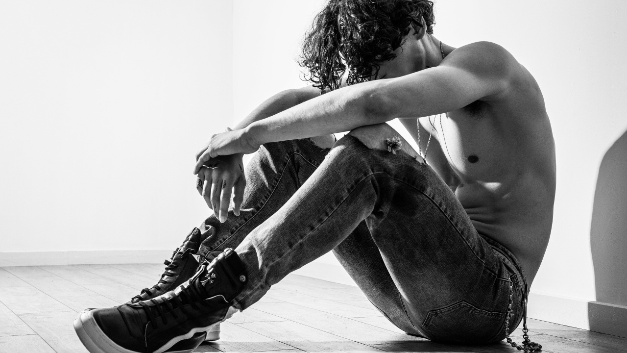 Грустный мужчина в джинсах сидит на полу