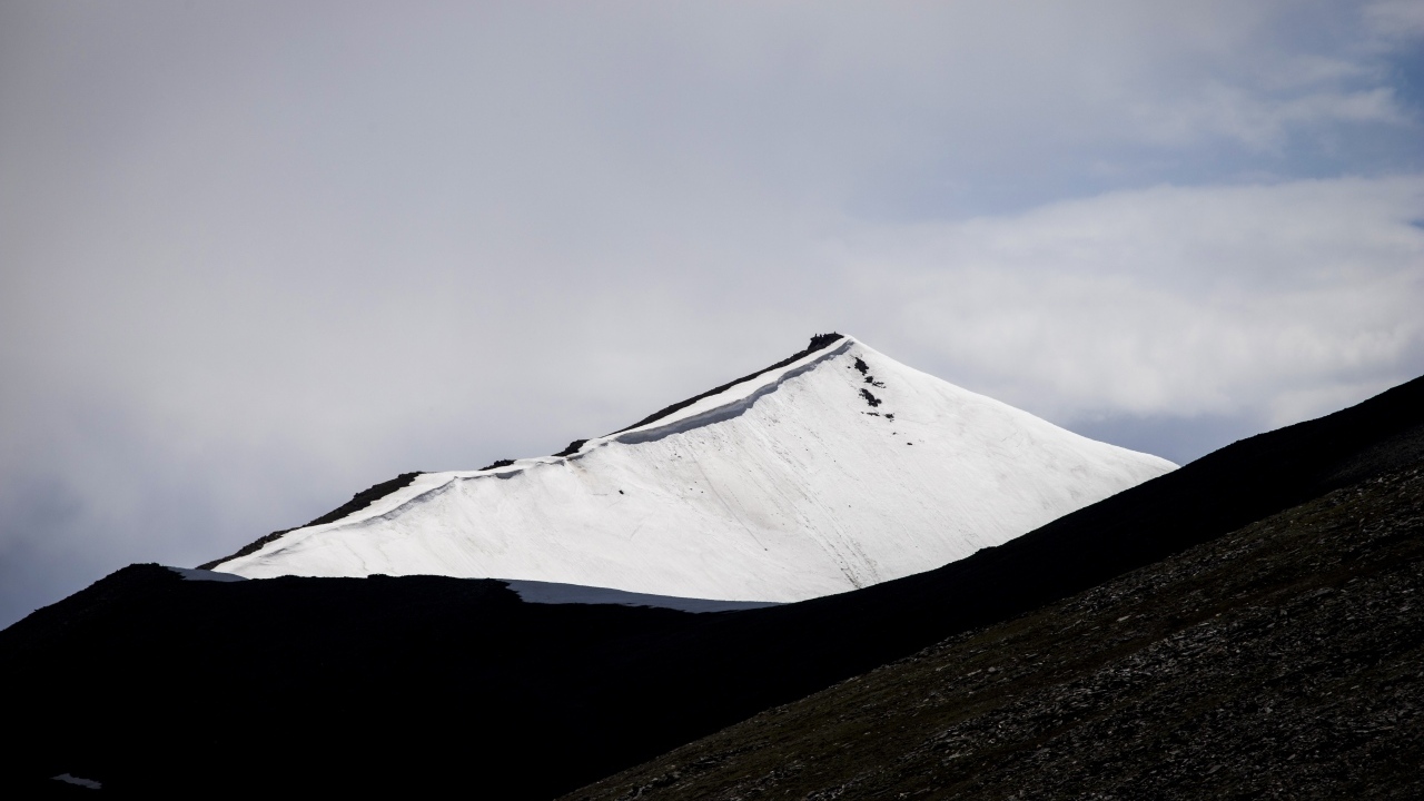 Заснеженная вершина горы под грозовым небом