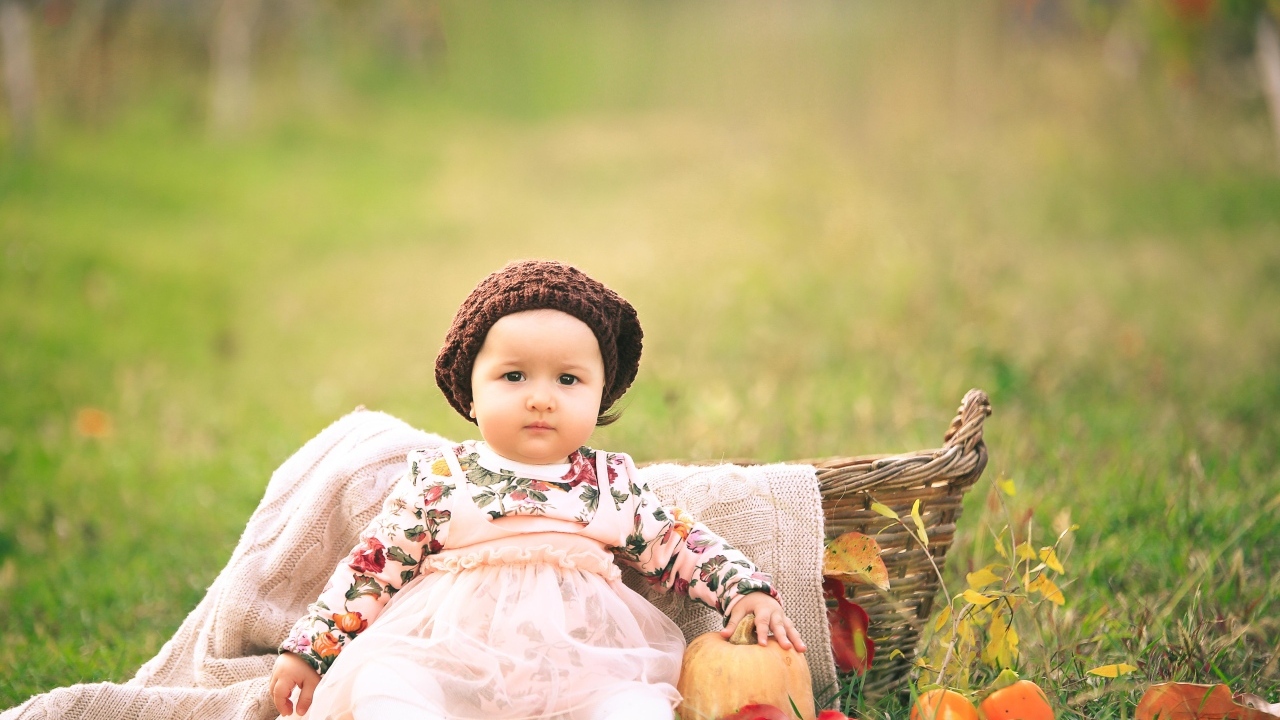 Милая маленькая девочка в шапке сидит на траве 