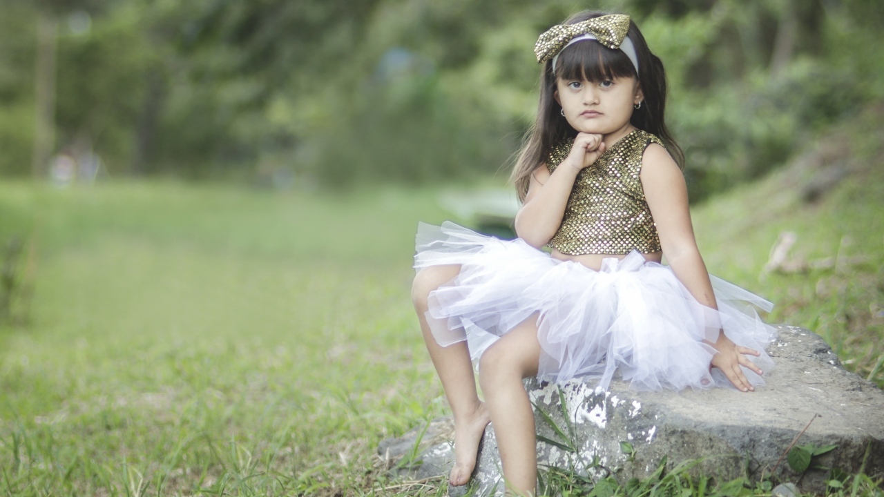 Девочка в красивом платье сидит на камне