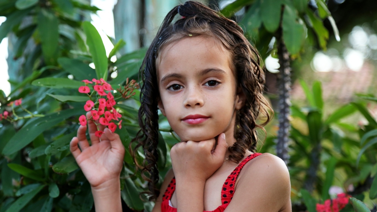 Девочка стоит у ветки с красными цветами