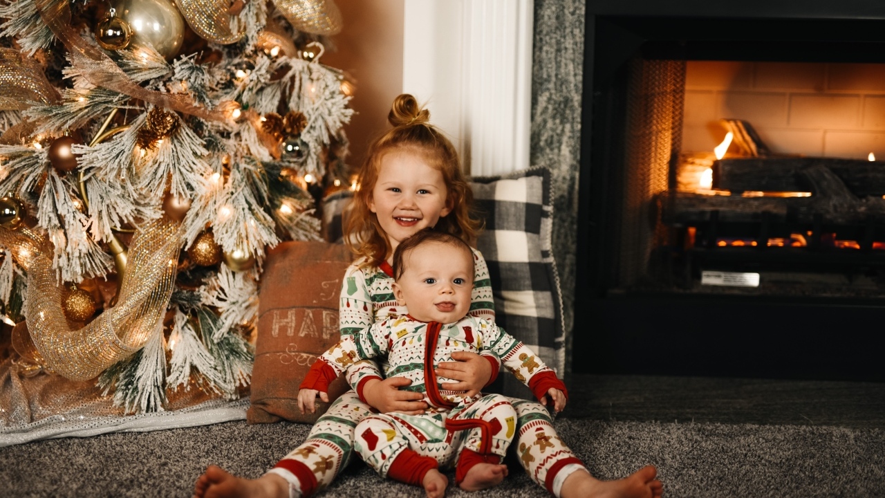 Маленькие брат и сестра сидят у новогодней ели